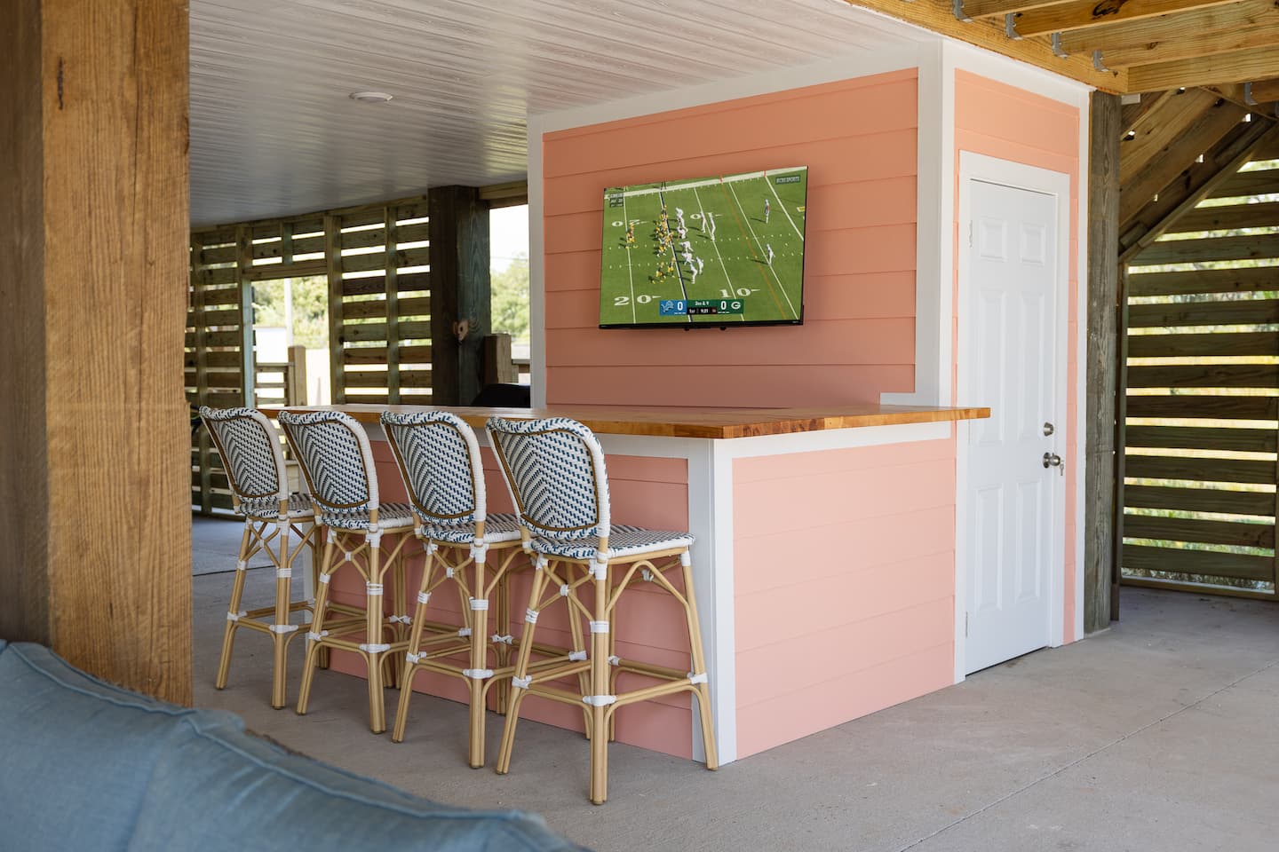 Covered poolside bar with woven stools and an outdoor television